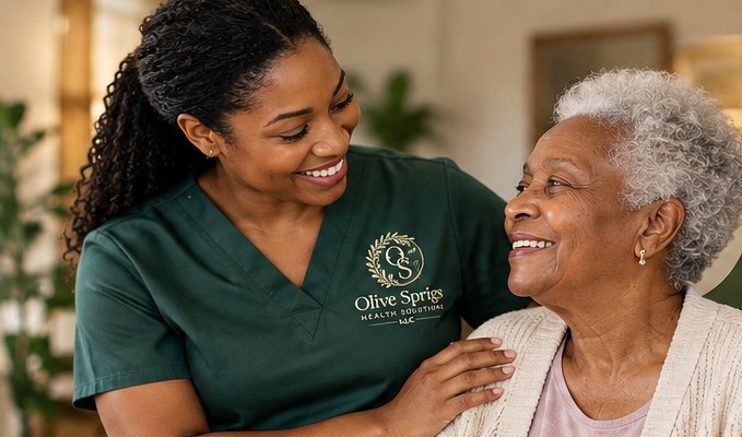 A smiling caregiver in olive scrubs with her arm around an older woman