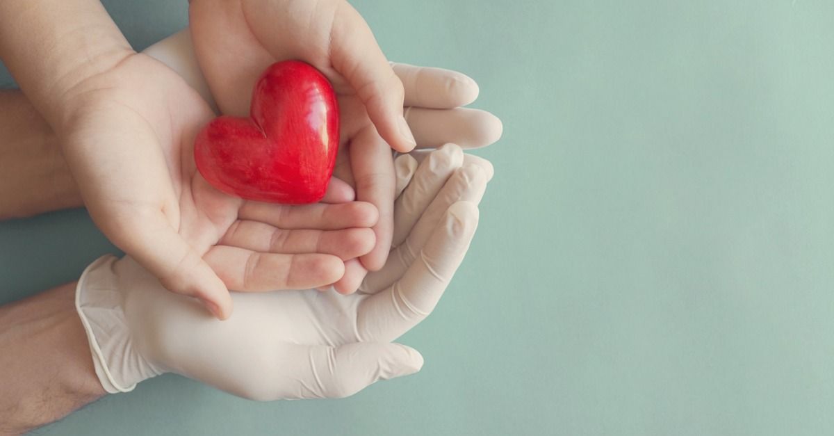 Gloved hands cradling a small red heart