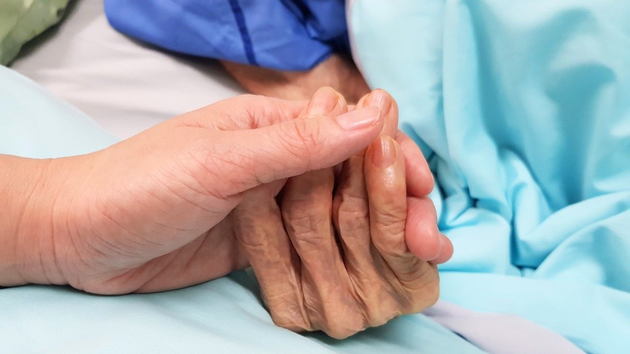 A caregiver gently holding the hands of a client resting in bed