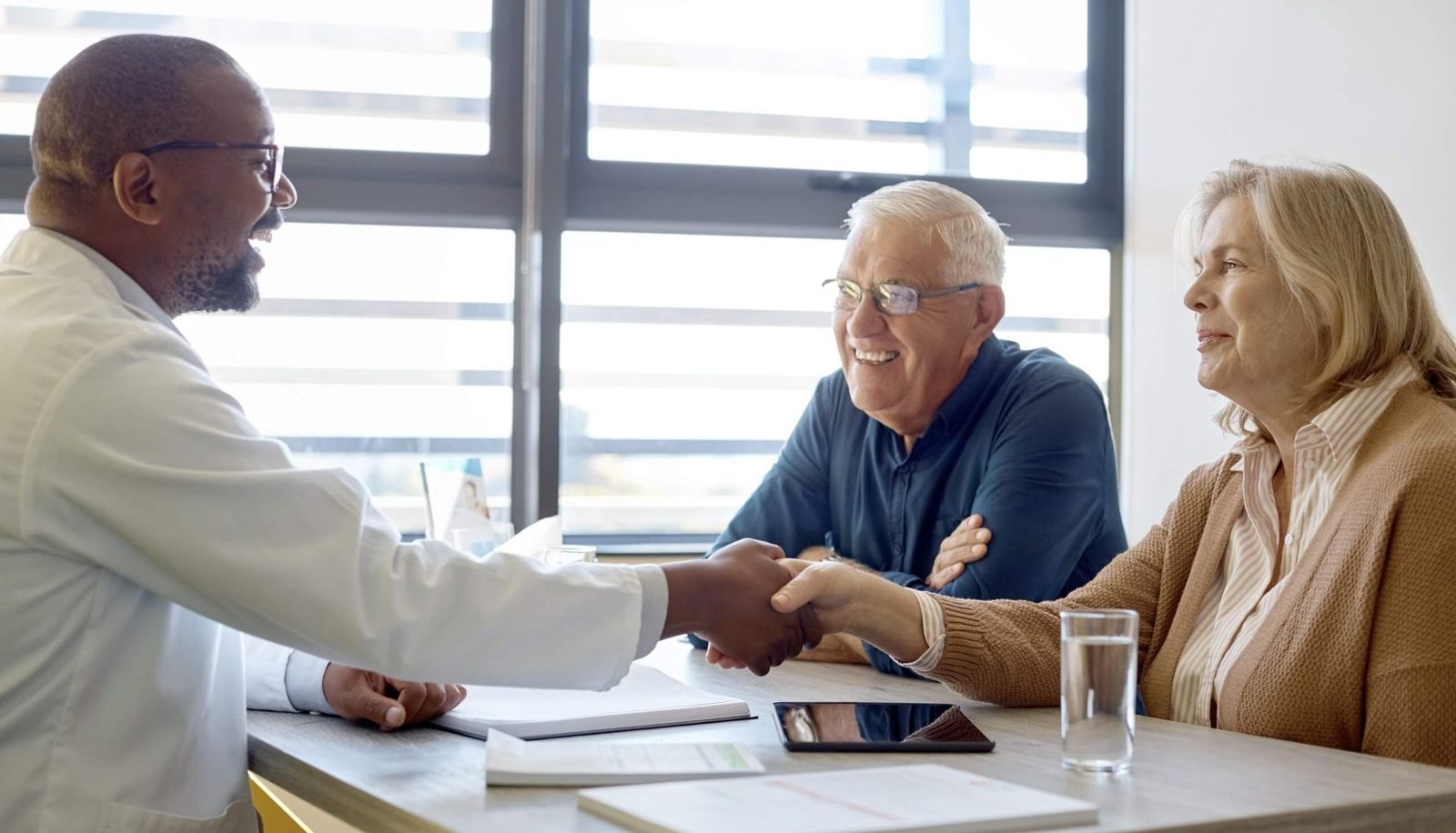 A care professional shaking hands with an older couple at a table