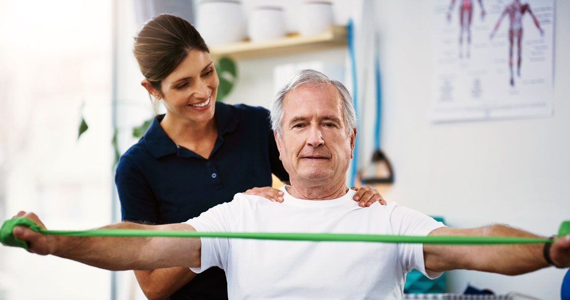 A caregiver guiding an older man through a resistance-band exercise